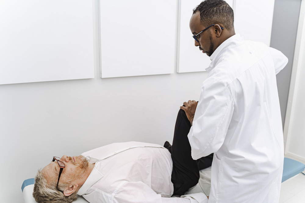 Lääkäri taivuttaa potilaan jalkaa.