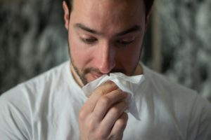 Mies potee flunssaa ja niistää nenäänsä.